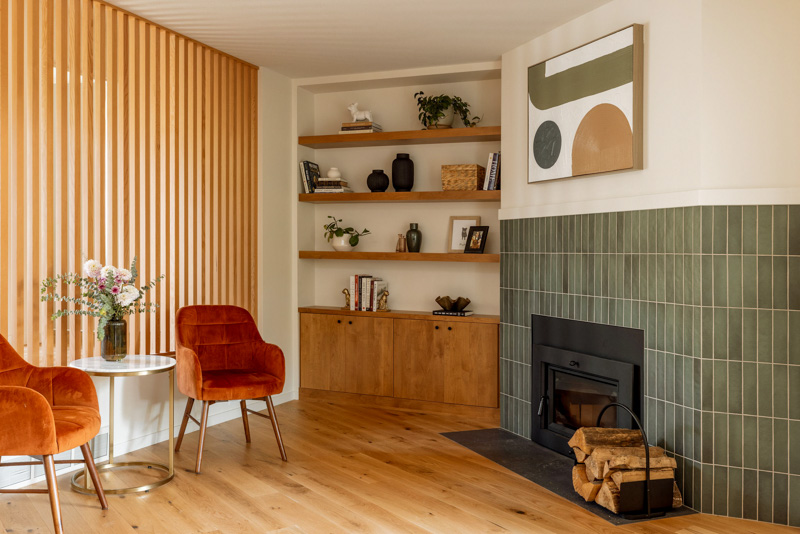 Modern living room remodel featuring a vertical wood slat wall, green tile fireplace surround, built-in shelving, and hardwood floors